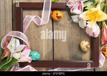 background from multi-colored flowers and painted eggs in frame with pink ribbon on wooden table. multicolored alstroemeria, pink, yellow, magenta Stock Photo