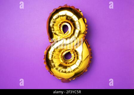 8 March. Happy Women's Day. Creative layout. Golden foil balloon number, digit eight 8. Birthday greeting card. Anniversary concept. Top view. Gold Stock Photo
