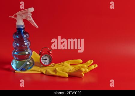 spray bottle and alarm clock and yellow gloves on a red background lie Stock Photo
