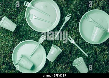 Environmental pollution. Disposable plastic tableware - plastic plates, forks, spoons, knives. Pastel plastic tableware on green grass, moss Stock Photo