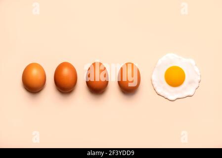four fresh brown eggs next to a fried egg on a beige background Stock Photo
