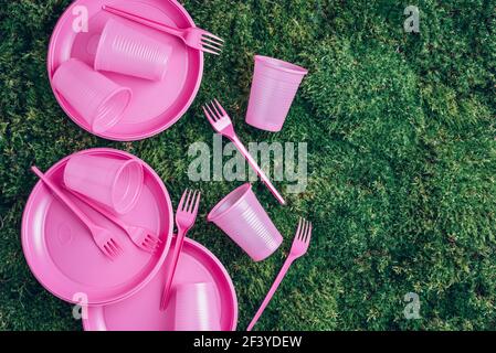 Pink plastic tableware on green grass, moss background. Top view. Copy space. Environmental pollution. Ban single use plastic. Disposable plastic Stock Photo