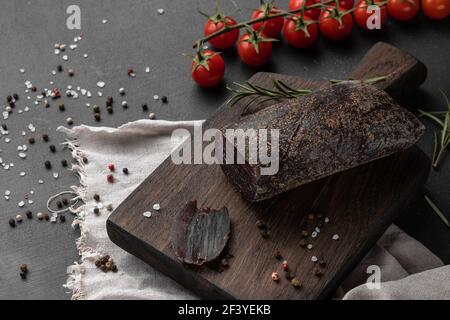 still life composition with a piece of red smoked dry ham of elk meat on a wooden cutting board, side view Stock Photo