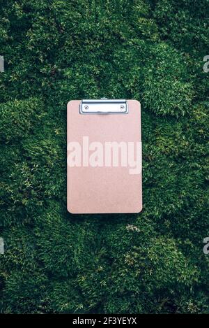 Top view of clipboard, paper, pen on green grass, moss background. Copy space. Flat lay. Office mock up, remote job. Wild nature, ecology concept Stock Photo