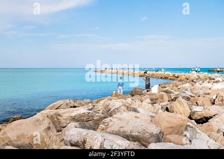 Venice, USA - April 29, 2018: Crowd of people men fishermen standing fishing on rocks of rocky Florida pier in retirement beach city in summer Stock Photo