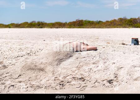 Sanibel Island, USA - April 29, 2018: Bowman's beach, Florida with funny young man buried under sand as mermaid with shells Stock Photo