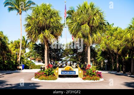 Naples, USA - April 30, 2018: Naples pier, Florida entrance sign with palm trees and American flag on flagpole in wealthy neighborhood community Stock Photo
