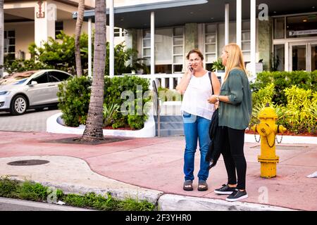 Miami Beach, USA - May 5, 2018: Women two friends standing on Collins avenue at Florida Art Deco South Beach district on street sidewalk by hotels in Stock Photo