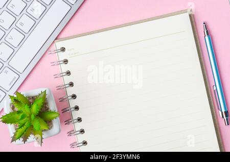 Open blank diary with keyboard computer on pink background. Stock Photo