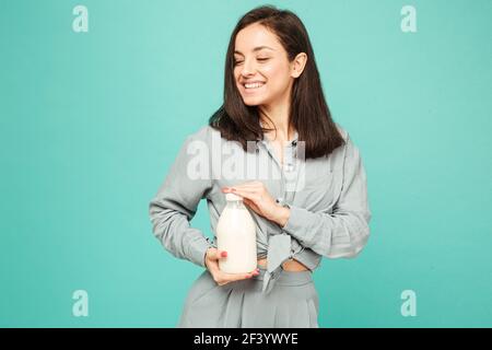 Photo of attractive lady holds bootle of milk, dairy products. Wears grey shirt, isolated turquoise color background Stock Photo