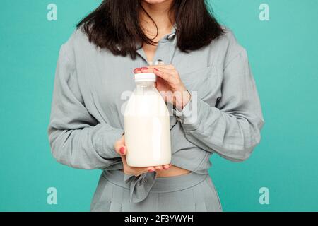 Photo of lady holds bootle of milk, dairy products. Wears grey shirt, isolated turquoise color background Stock Photo