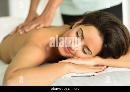 Young female receiving a relaxing back massage in a spa center. Brunette woman patient is receiving treatment by professional therapist. Stock Photo