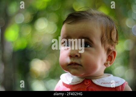 Close-up portrait of six months old baby girl looking at something outdoors with defocused background. Stock Photo