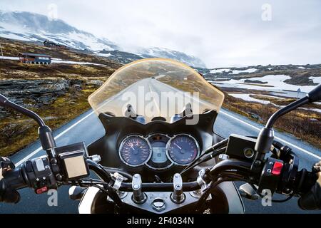Biker First-person view, mountain pass in Norway. Biker rides a motorcycle on a slippery road through a mountain pass in Norway. Around the fog and snow. First-person view. Stock Photo