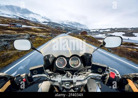 Biker First-person view, mountain pass in Norway. Biker rides a motorcycle on a slippery road through a mountain pass in Norway. Around the fog and snow. First-person view. Stock Photo