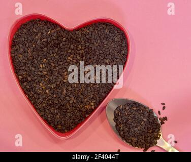 Black sesame seeds in the shape of a heart on a pink background, top view. Healthy food, vegan product concept Stock Photo