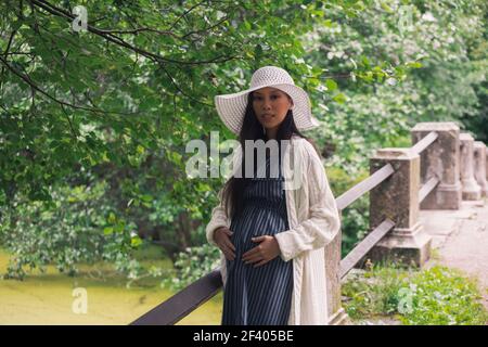 Young asian pregnant woman in white hat near bridge Stock Photo