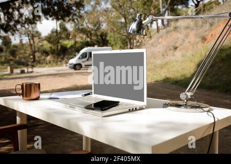 digital nomad work table in the field,with campervans in the background. Mockups computer screen for text and image. Stock Photo