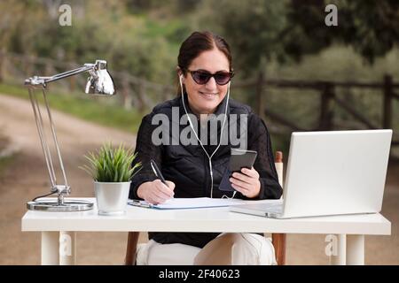 Freelance woman works in outdoor office, with computer at table. Nominated digital and telecommuning concept Stock Photo