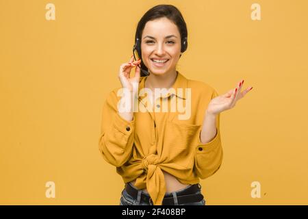 Photo of cute female with headphones and talking on microphone. Wears yellow shirt, isolated yellow color background Stock Photo