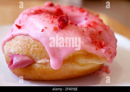 Closeup of mouthwatering strawberry-glazed with raspberry cream filling doughnut on a white plate Stock Photo