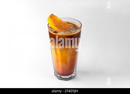 transparent glass of yellow refreshing summer drink with sliced orange, ice cubes and chocolate syrup isolated on a white and gray background with nat Stock Photo