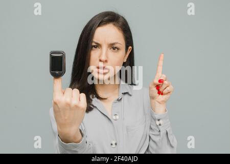 Close up photo female with pulse oximeter on her finger, checks her health. Wears grey dress, isolated grey color background Stock Photo