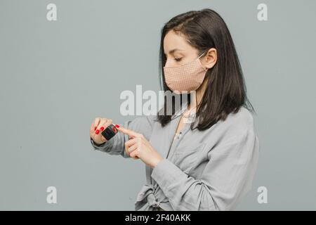 Photo female in face mask with pulse oximeter on her finger, checks her health. Wears grey dress, isolated grey color background Stock Photo