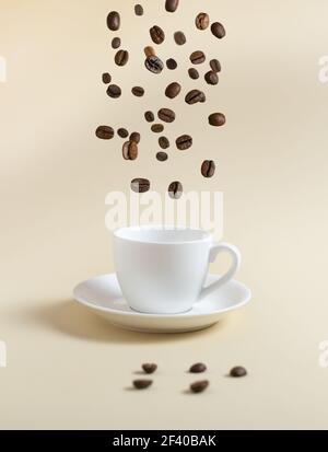 Coffee beans are flying into a white espresso cup on a yellow background. Flying food concept. Stock Photo