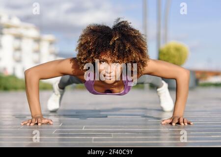 Black fit woman doing pushups on urban floor. Young female working out in the street. Stock Photo