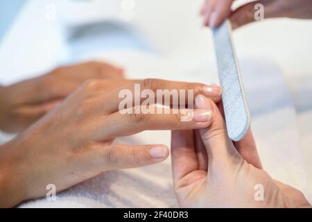 Close-up of a woman in a nail salon receiving a manicure by a beautician with. Beautician file nails to a customer. Stock Photo