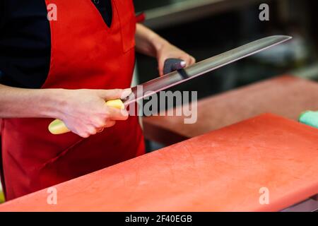 Young female butcher sharpening a knife in a butcher shop Stock Photo