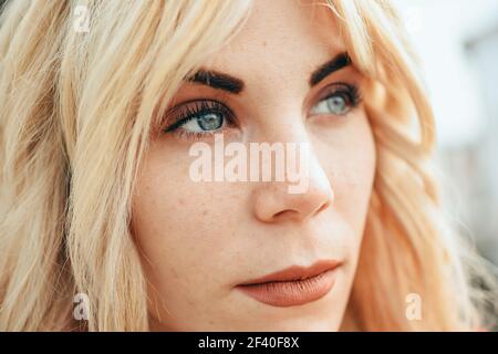 Close-up portrait of happy young blond woman sitting outdoors. Blonde girl with beautiful blue eyes. Stock Photo