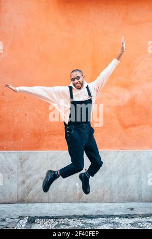 Young black man wearing casual clothes jumping in urban background. Lifestyle concept. Millennial african guy with bib pants outdoors Stock Photo