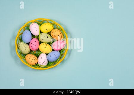Multicolored Easter eggs in a plastic basket on a blue background. Place for an inscription. View from above. Easter. Stock Photo