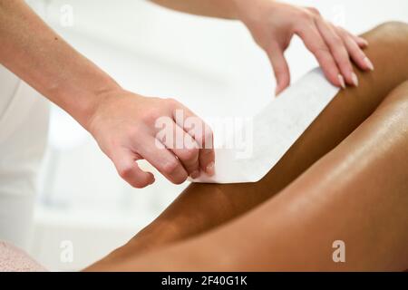 Woman having hair removal procedure on leg applying wax strip depilatory in salon. Depilation concept Stock Photo