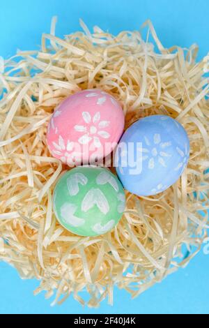 Colorful handmade painted Easter eggs in the nest on a blue background. Easter eggs decorated by a child. Top view, vertical shot Stock Photo
