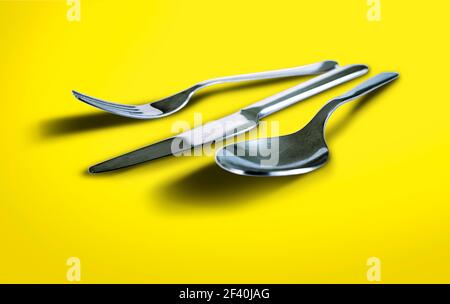 Fork spoon and knife isolated on yellow bright background Stock Photo