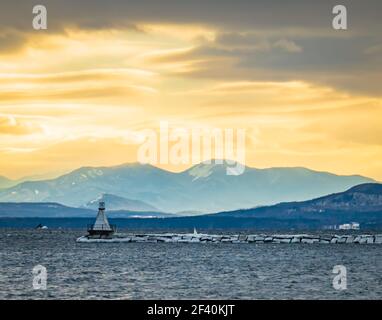 sun setting on Lake Champlain breakwater's lighthouse with the Adirondack mountains in New York across the lake Stock Photo