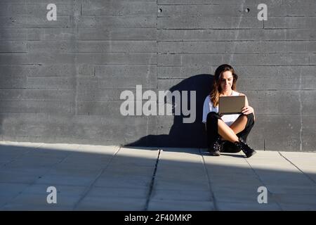 Young businesswoman working with her laptop computer sitting on the floor outdoors.. Middle-age businesswoman working with her laptop computer sitting on the floor. Stock Photo