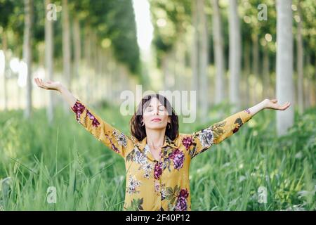 Enjoying the nature. Young woman arms raised enjoying the fresh air in green forest. Female with eyes closed.. Woman arms raised enjoying the fresh air in green forest. Stock Photo