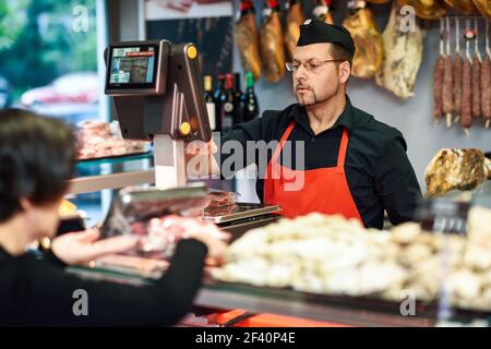 Butcher attending a customer in a butcher&rsquo;s shop weighing the meat and charging. Butcher attending a customer in a butcher&rsquo;s shop Stock Photo
