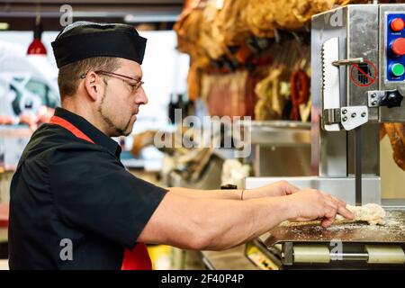 Male butcher cutting ham bones in a cutting machine inside a butcher shop.. Male butcher cutting ham bones in a cutting machine Stock Photo