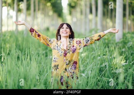 Enjoying the nature. Young woman arms raised enjoying the fresh air in green forest. Female wearing flowered dress.. Woman arms raised enjoying the fresh air in green forest Stock Photo