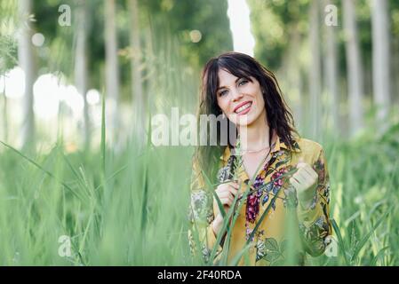 Beautiful hiker young woman, wearing flowered dress, hiking in the countryside.. Young woman, wearing flowered dress, between trees. Stock Photo