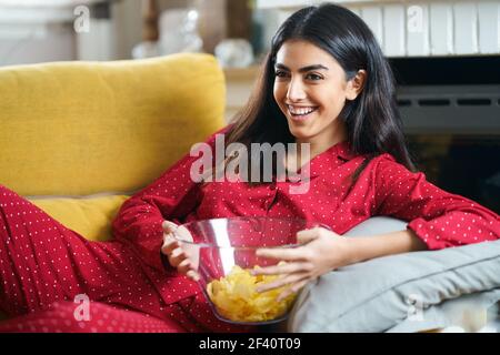 Persian woman at home watching TV. Girl eat chips potatoes. Persian woman at home watching TV eating chips potatoes Stock Photo