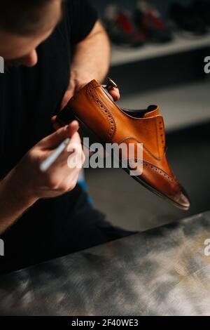 Top view of shoemaker painting heel and sole of light brown leather shoes with brush during restoration working. Stock Photo