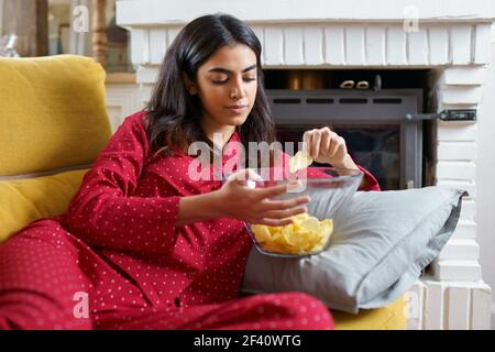 Persian woman at home watching TV. Girl eat chips potatoes. Persian woman at home watching TV eating chips potatoes Stock Photo