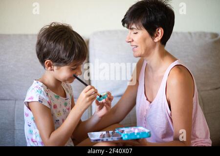 Happy beautiful mother and her little cute daughter doing make up for each other. Mum spending free time with her daughter.. Mother and her little daughter doing make up for each other Stock Photo