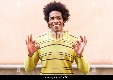 Black man with afro hair putting a funny expression outdoors. Ok gesture with his hands. Black man with afro hair putting a funny expression Stock Photo